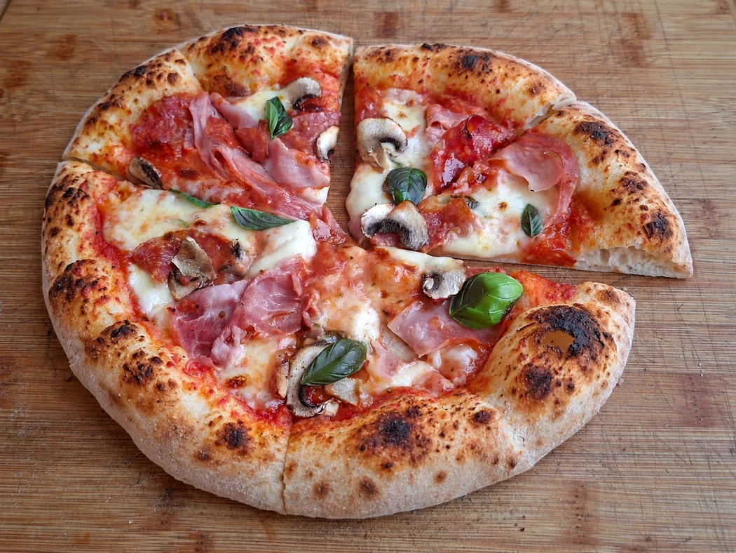 Angeschnittene Pizza mit Schinken, Champignons und Basilikum